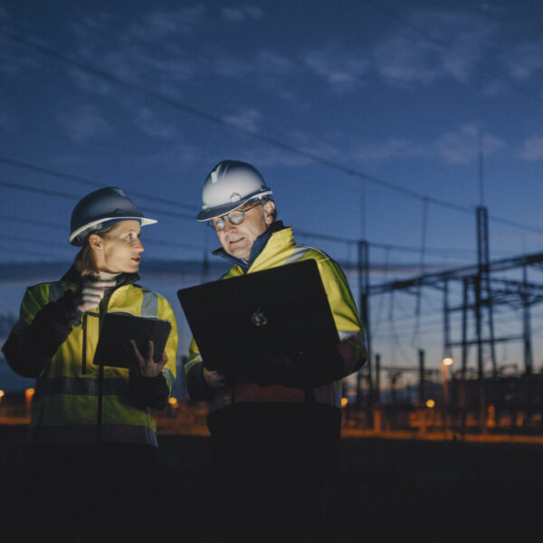 At a dark power station in the still of night,electrical engineers engage in discussions over a laptop and digital tablet,blending technology seamlessly in their collaborative work
